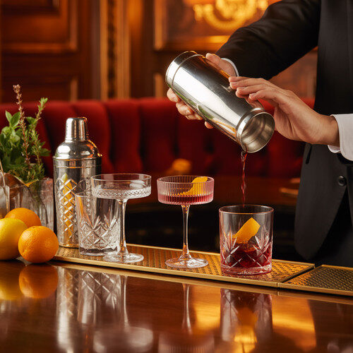 alt_text: An elegant bar scene showcasing diverse cocktails, vintage tools, and fresh ingredients in soft light.